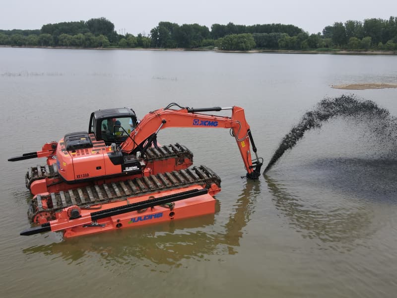 Mit Pontons ausgestatteter Amphibienbagger arbeitet im See/Fluss